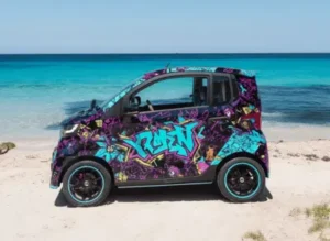 Bunt gestalteter Skyliner TS Shary Mobil im Graffiti-Design am Strand vor türkisblauem Meer.