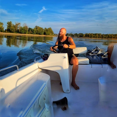 Pätrick Triebel, Gründer der Water Punk Akademy, steuert ein Boot auf einem Fluss und steht für die Verbindung von Natur, Wasser und bewusstem Leben.